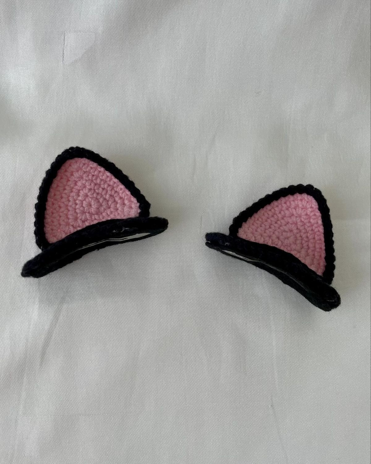 Handmade black and pink crochet cat ear hair clips set on neutral fabric background.