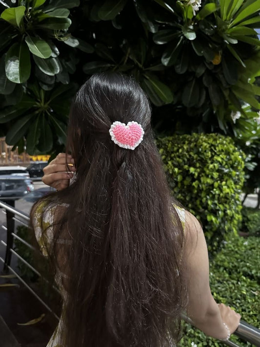 Handmade pink and white crochet heart hair clip styled on long dark hair outdoors