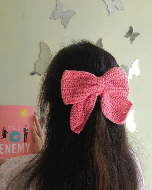 Large handmade pink crochet bow hair clip styled on long dark hair.