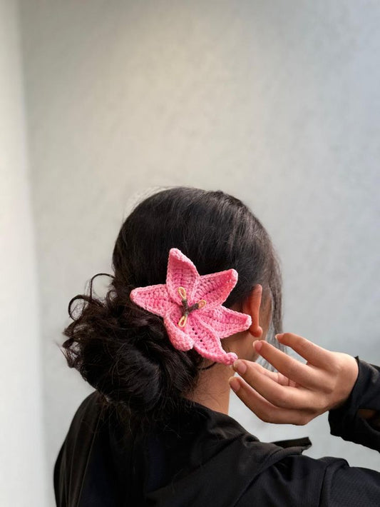 Handmade pink crochet lily flower hair clip worn in a bun hairstyle